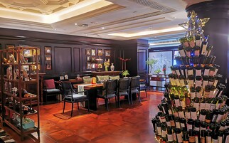 Un restaurante con una larga mesa de comedor, sillas y una exhibición de vinos.