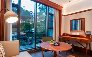 Una habitación de hotel moderna con un ventanal grande, una mesa redonda de madera, un sofá, un escritorio y un espejo.