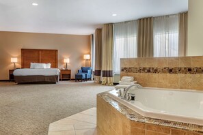 Een hotelkamer met een groot bed, een apart zithoekje met een stoel en tafel, een badkamer met bad en een raam met gordijnen.