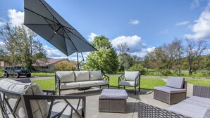 An outdoor patio with wicker furniture, a large umbrella, and a Jeep in the background.