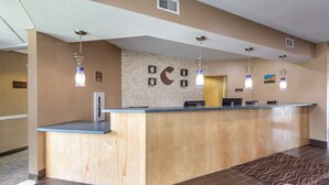 A reception desk with a wooden finish, a wall-mounted clock, and pendant lighting.