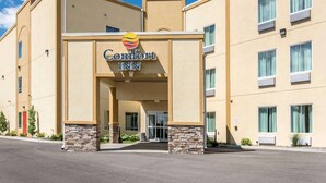 A Comfort Inn hotel with a beige facade, stone pillars, and a clear blue sky.