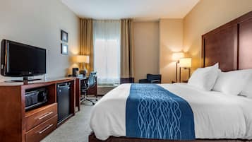 A hotel room with a large bed, a television, a desk with a chair, and a desk lamp.