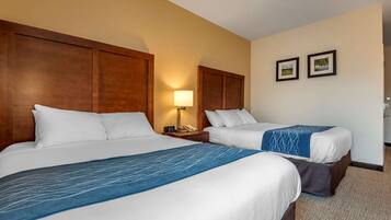 A hotel room with two beds, a nightstand with a lamp, and two framed pictures on the wall.