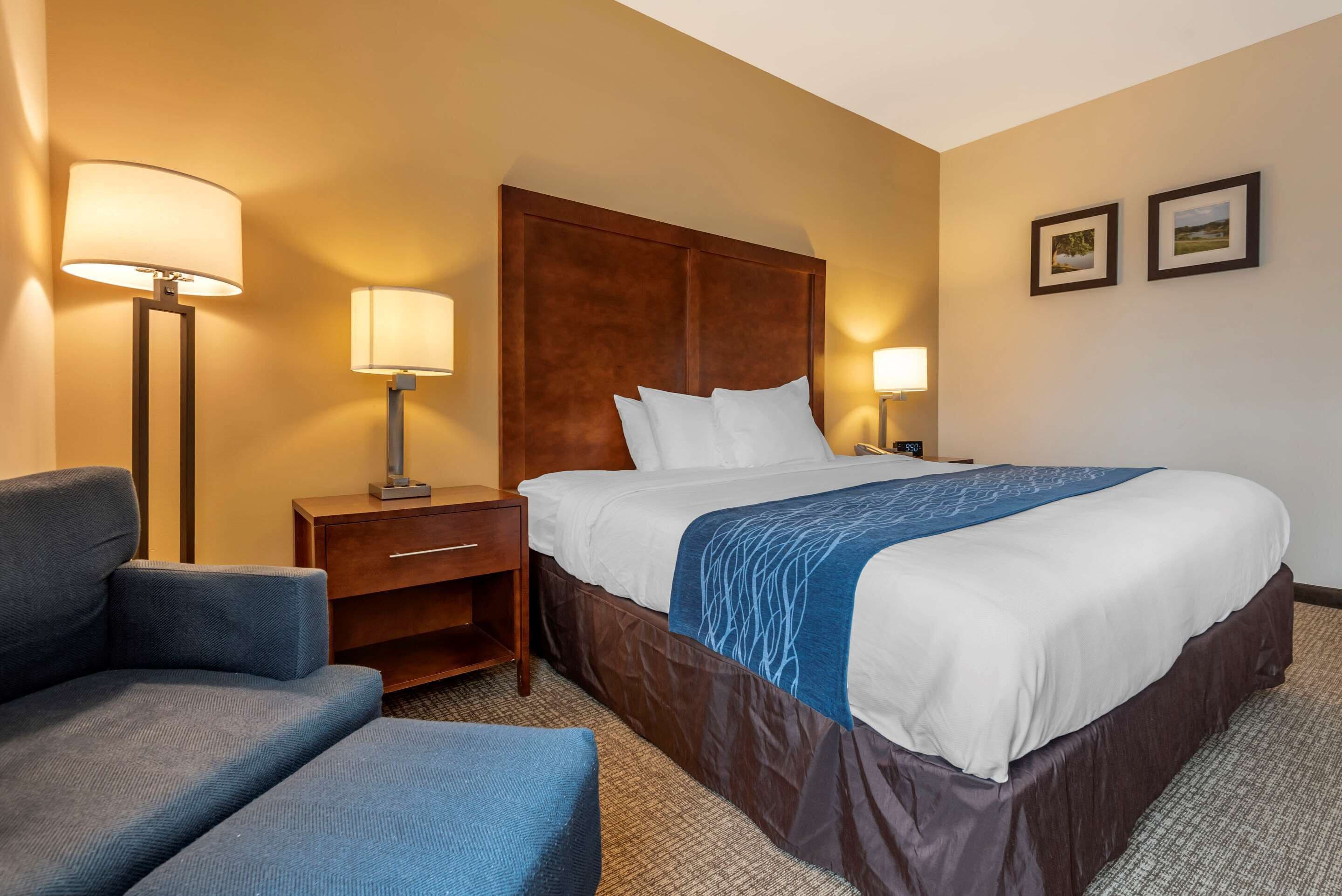 A hotel room with a large bed, a nightstand, a desk, a chair, and two wall-mounted lamps.