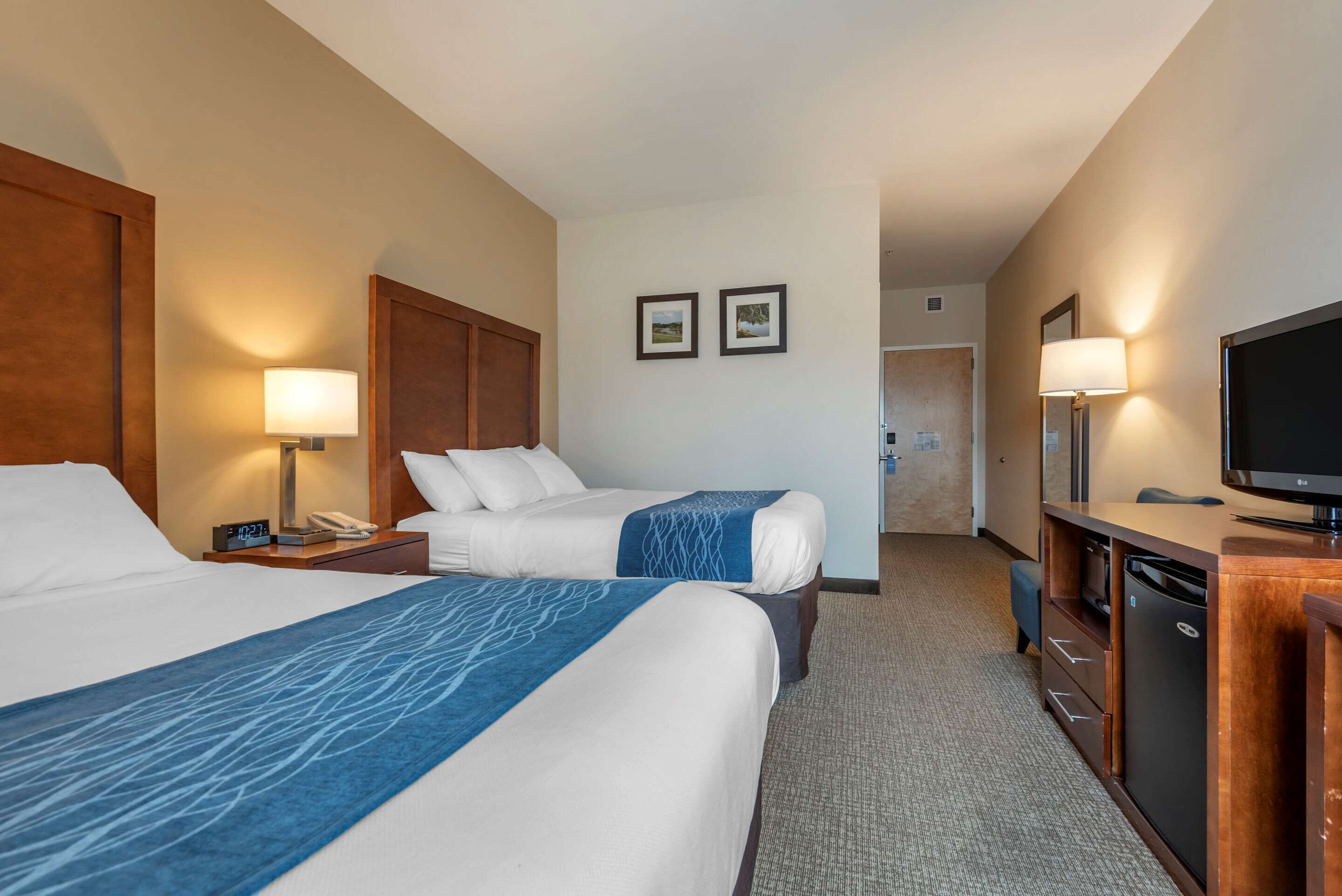 A hotel room with two beds, a desk with a television, and a small kitchenette.