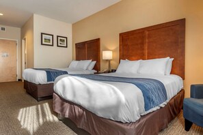 A hotel room with two beds, a desk, a chair, and a door.