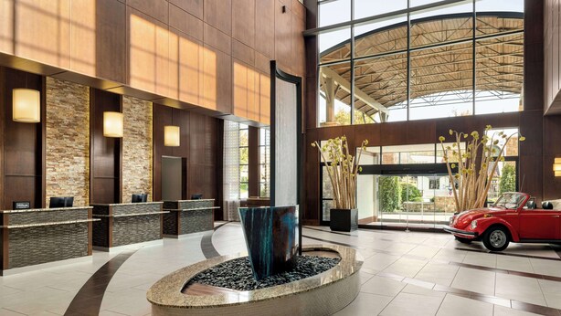 A modern lobby with a reception desk, a unique water feature, and a vintage car. - Embassy Suites Chattanooga / Hamilton Place (Chattanooga)