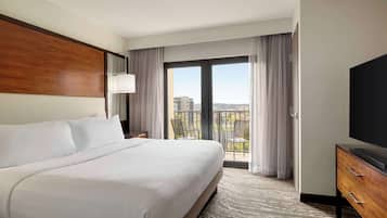 A hotel room with a large bed, a TV, a balcony with curtains, and a view of the city.