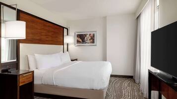 A hotel room with a bed, a desk with a lamp, a television, and a painting on the wall.