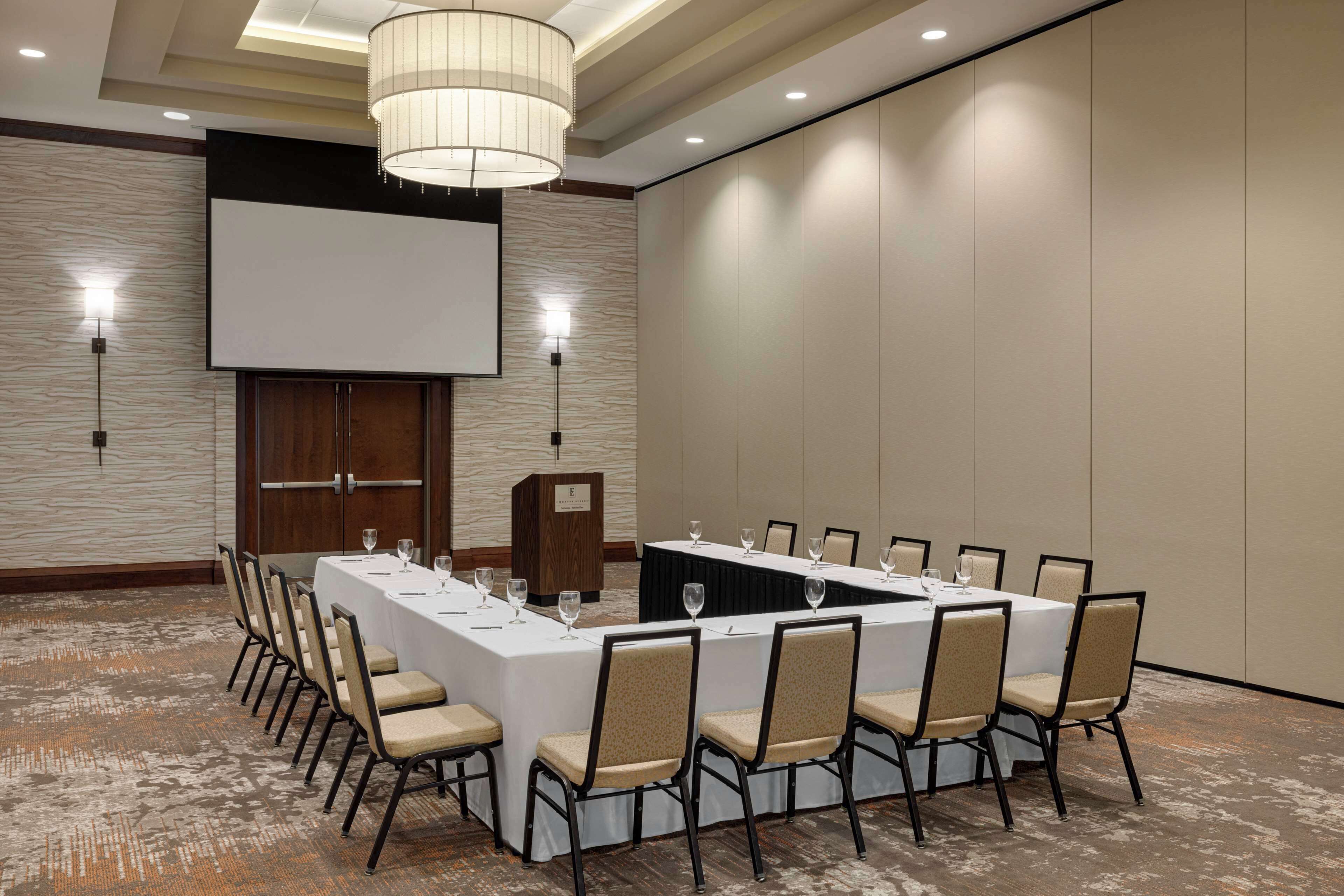Une salle de conférence équipée d’une longue table, de chaises, d’un pupitre et d’un écran de projection.