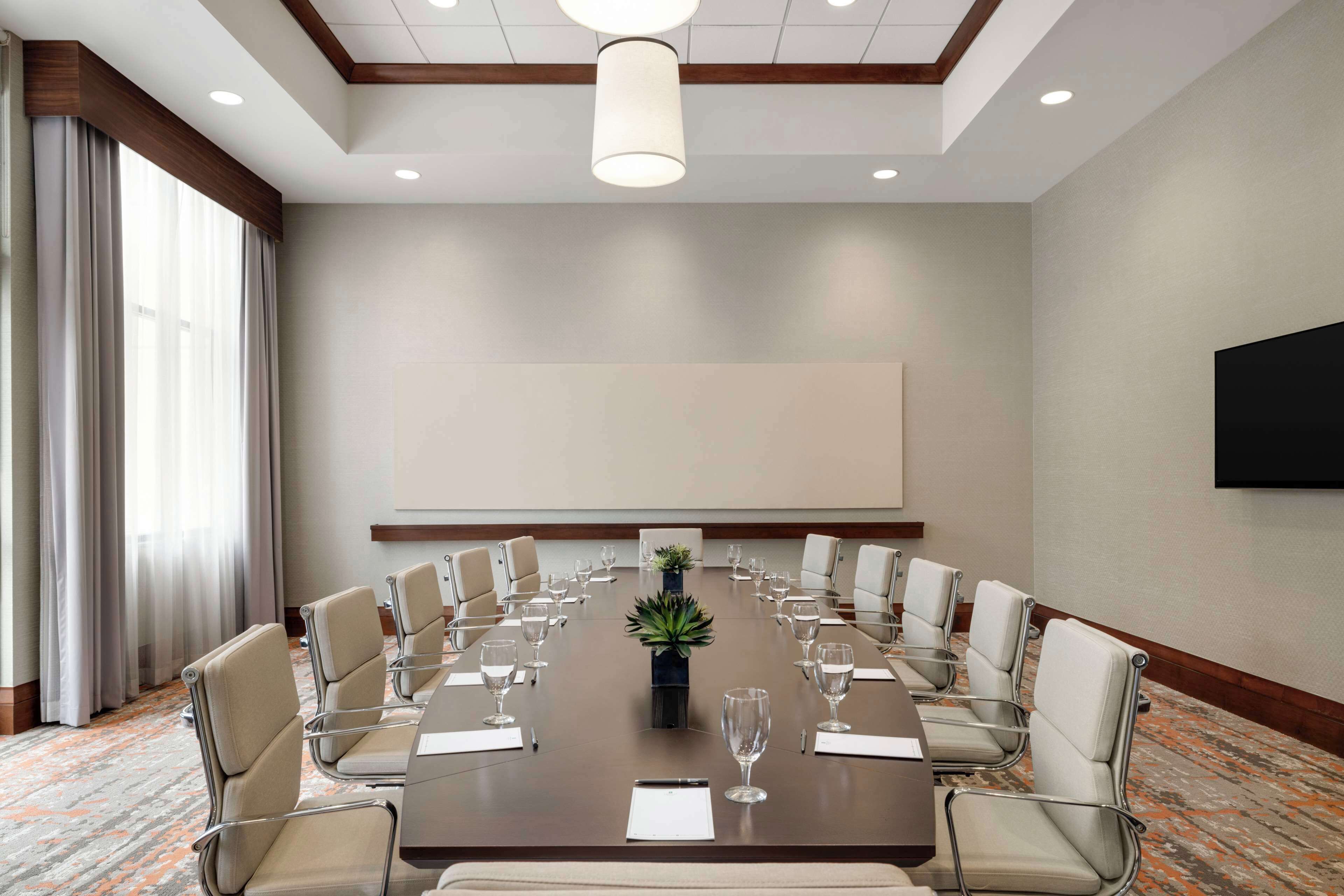 Une salle de conférence avec une longue table, des chaises de couleur beige, un écran de projection et une plante servant de décoration centrale.