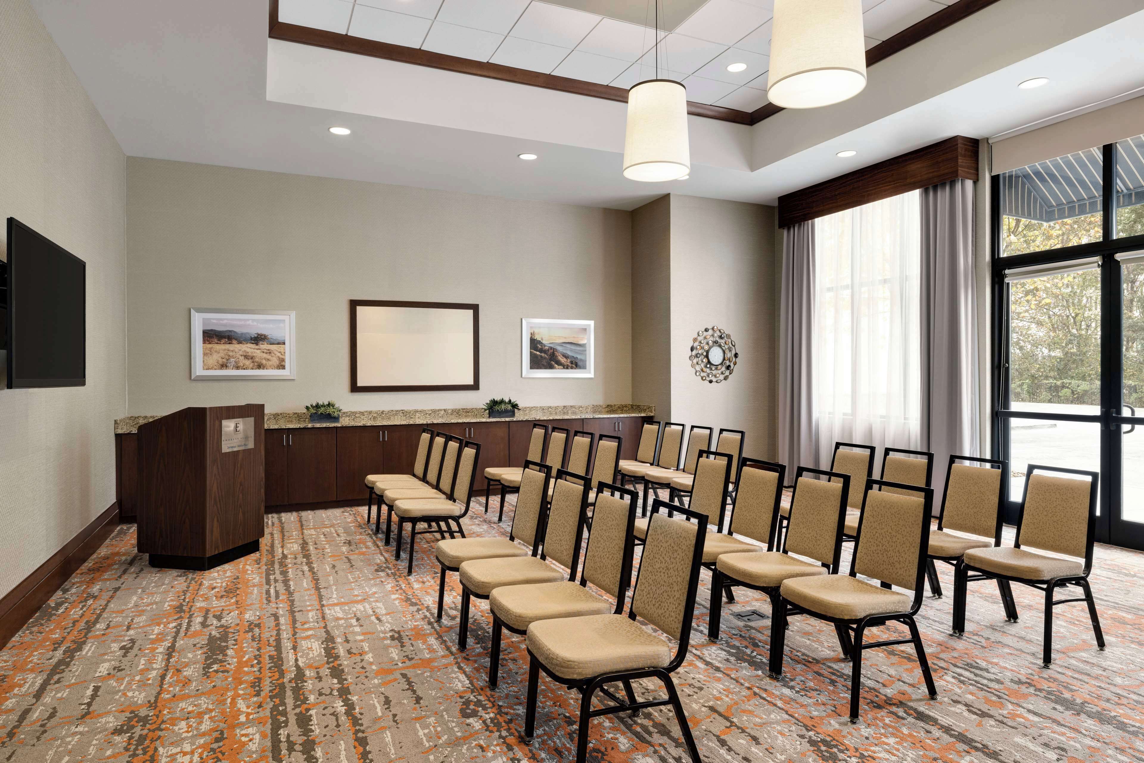A conference room with a long table, chairs, a podium, and framed pictures on the wall.