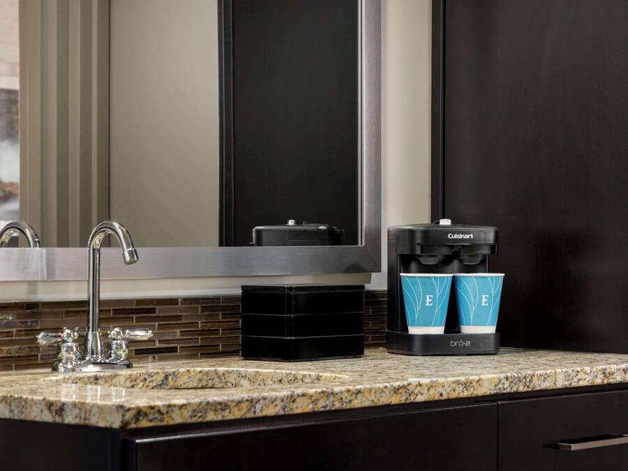 A modern bathroom with a granite countertop, a black coffee maker, and a coffee pod holder.