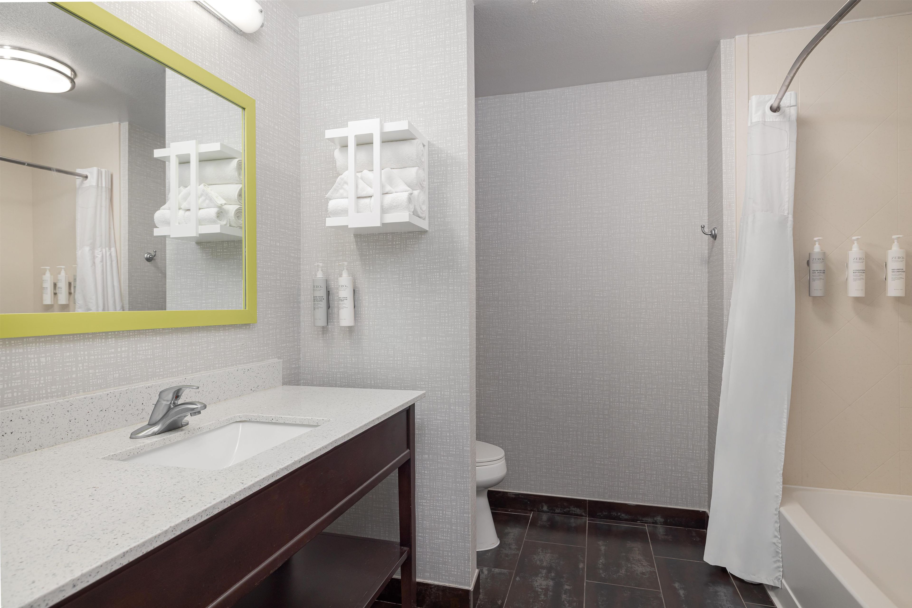 A bathroom with a white sink, mirror, and towel rack. There is a shower curtain and a toilet visible.