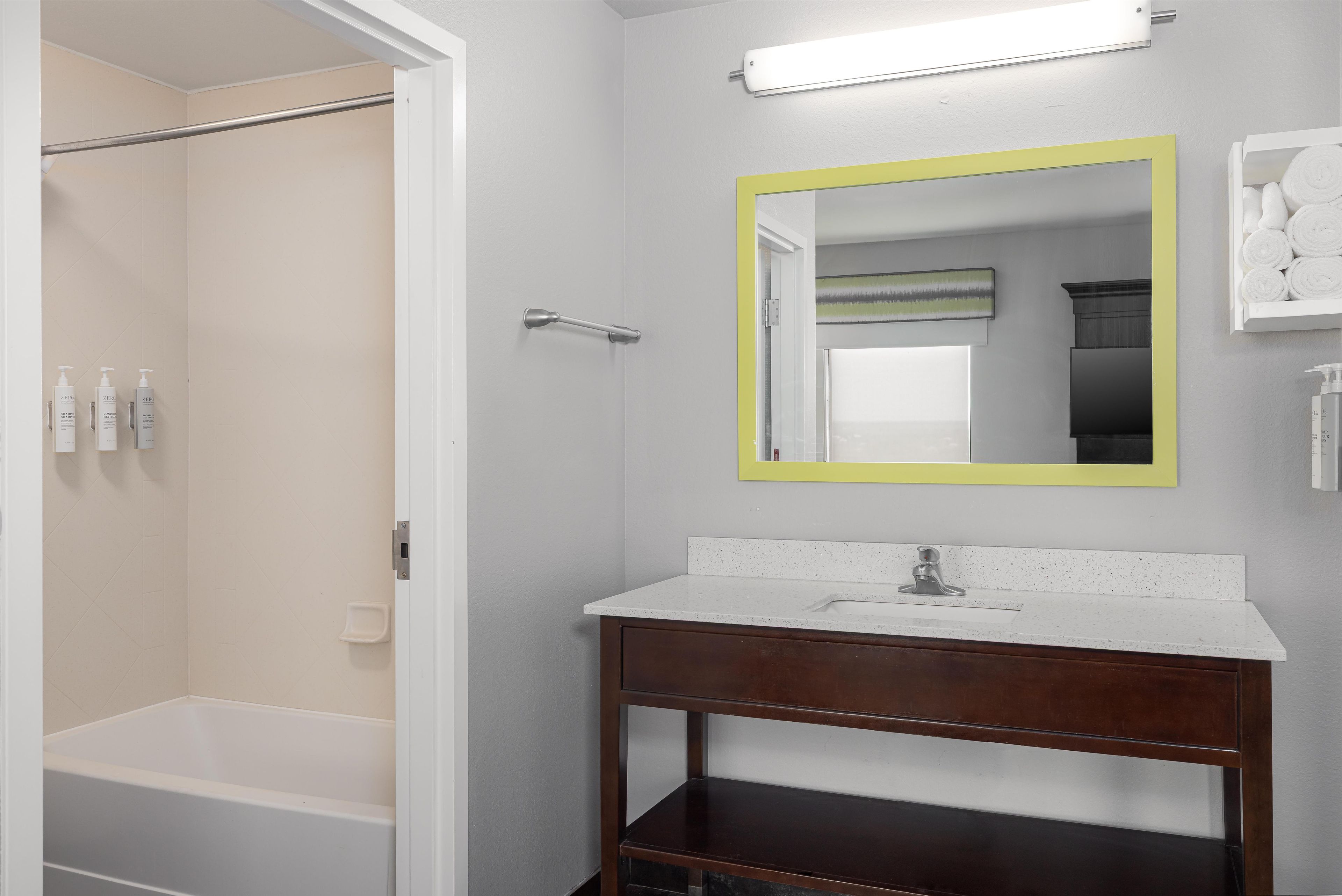 A bathroom with a white bathtub, a wooden vanity, a mirror with a yellow frame, and a towel rack with towels.