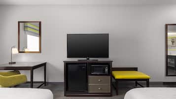 A hotel room with a flat-screen TV, a minibar, a desk with a lamp, two beds, and a mirror.