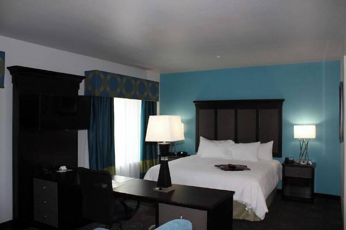 Una habitación de hotel con cama, escritorio, silla, lámparas y televisor.