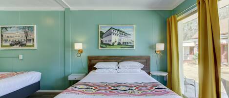 Una habitación de hotel con una cama, dos mesitas de noche, un ventilador de techo y una ventana con cortinas.