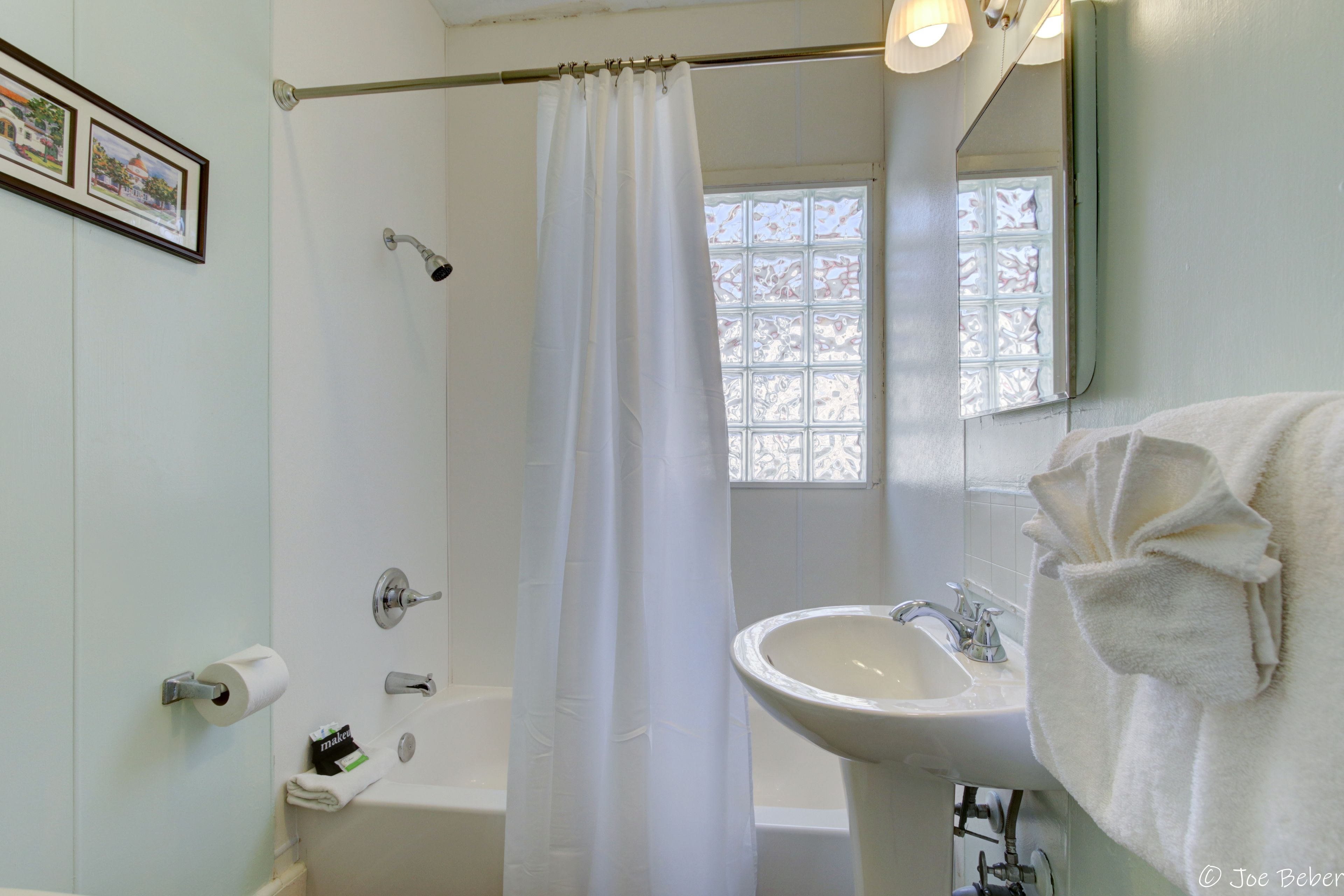 A bathroom with a bathtub, a sink, a shower curtain, a toilet paper holder, and a window with a view.