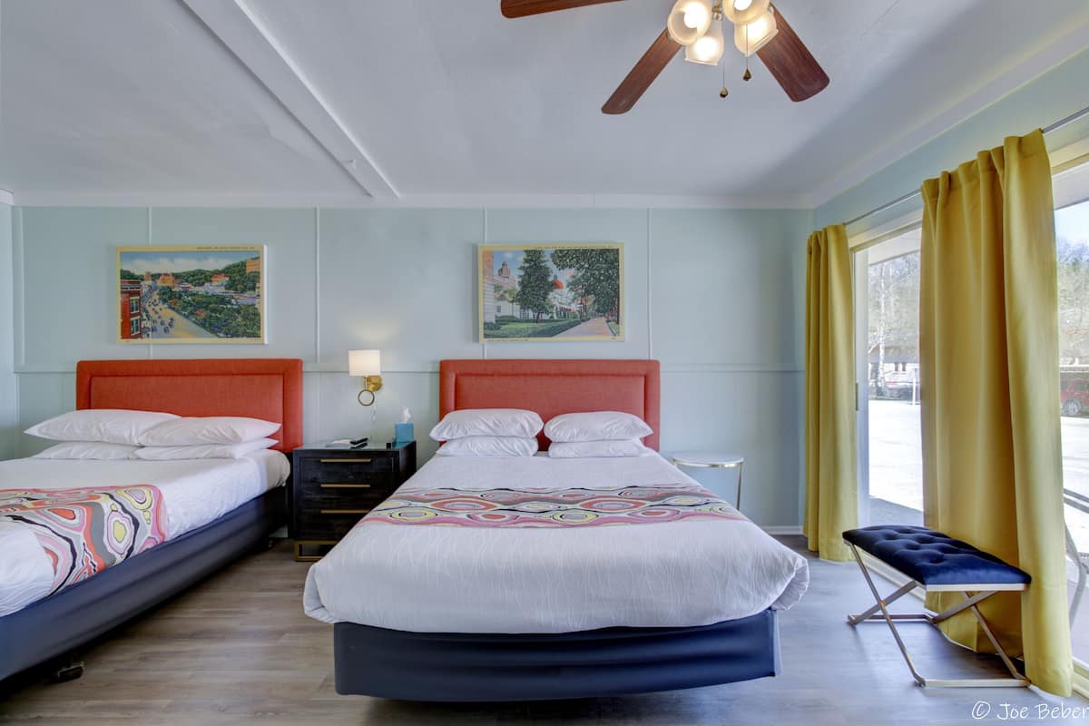 A double room with two beds, a ceiling fan, and artwork on the walls.