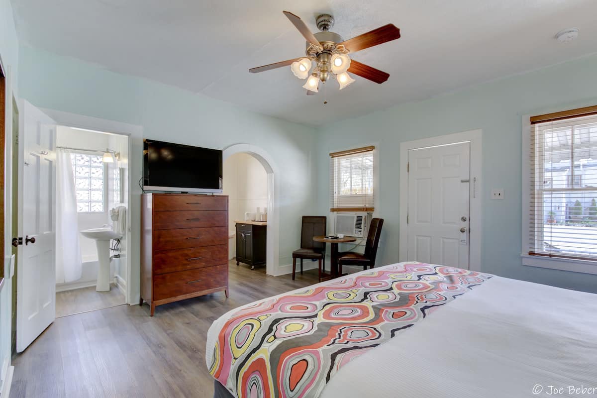 A bedroom with a bed, a ceiling fan, a dresser, a television, a desk, and a window.