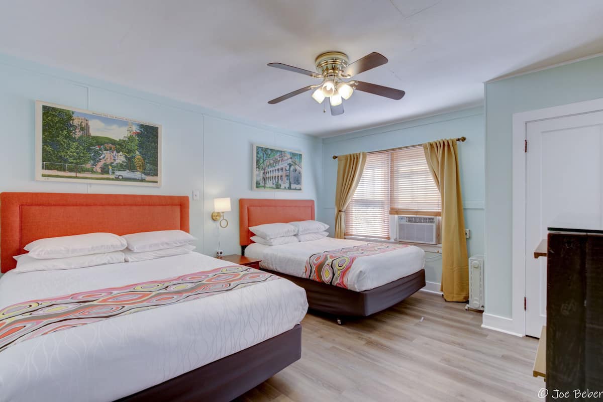 A hotel room with two beds, a ceiling fan, and artwork on the walls.