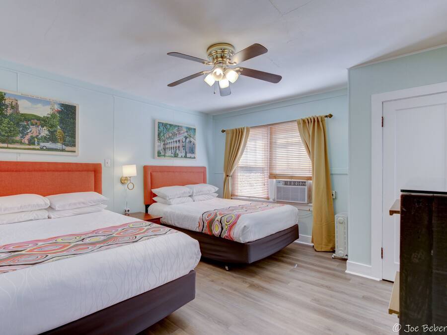A hotel room with two beds, a ceiling fan, and artwork on the walls.