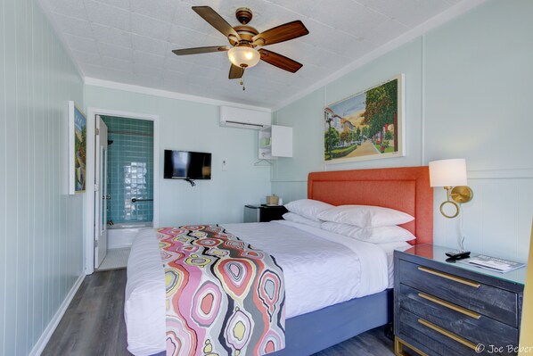 A bedroom with a bed, a ceiling fan, a nightstand, a TV, and a painting on the wall.