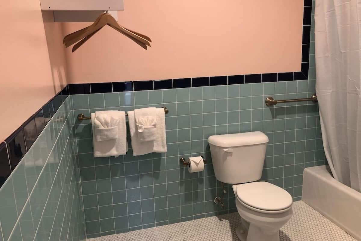A bathroom with a toilet, a towel rack with towels, a shower curtain, and blue-tiled walls.