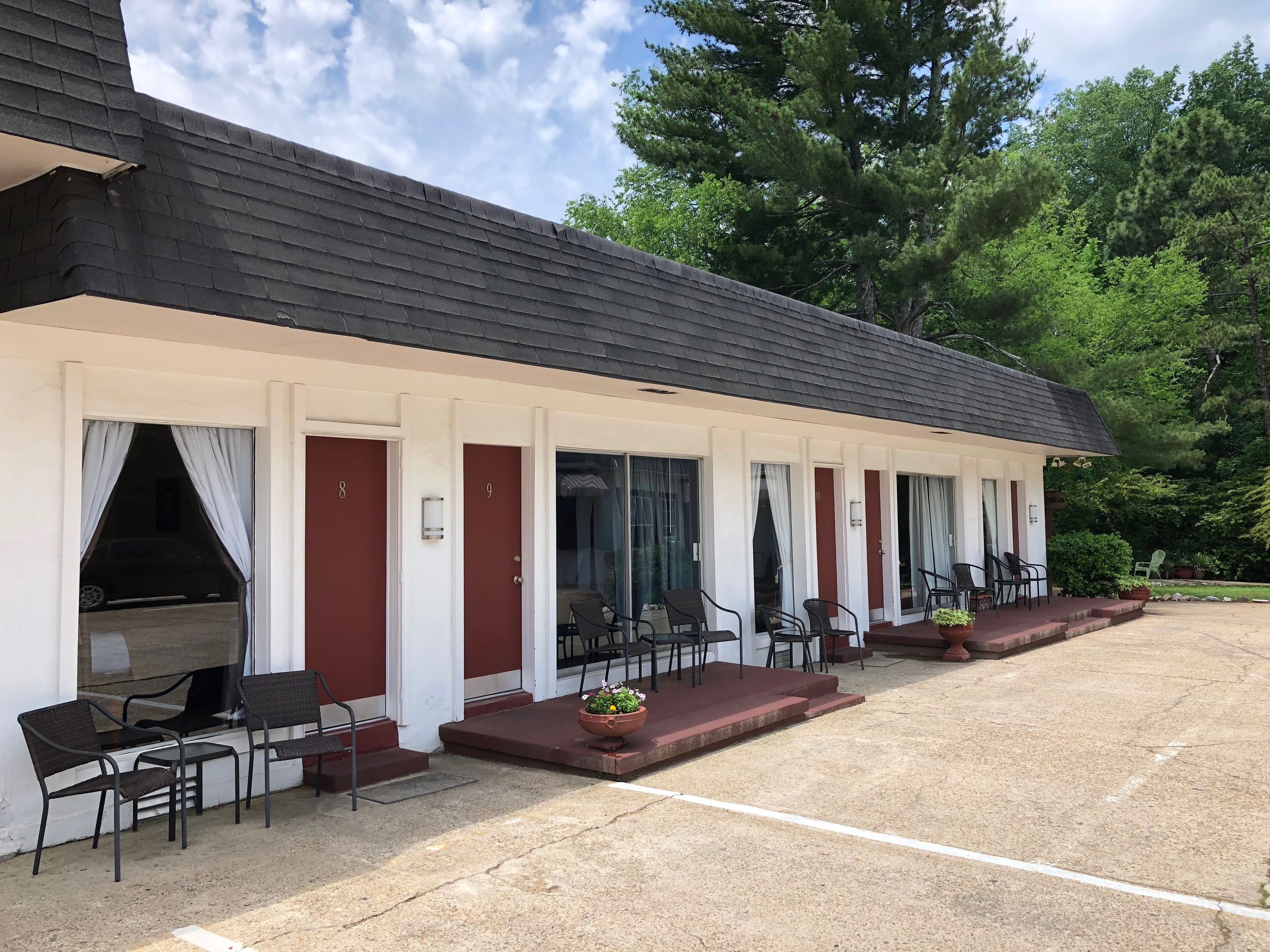 A motel with a covered front porch, numbered rooms, and outdoor seating.