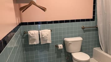 Un baño con inodoro, dos toallas en un perchero, cortina de ducha y suelo de baldosas.