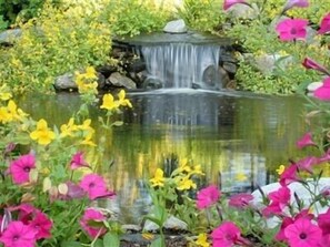 A garden with a small waterfall, surrounded by pink and yellow flowers.