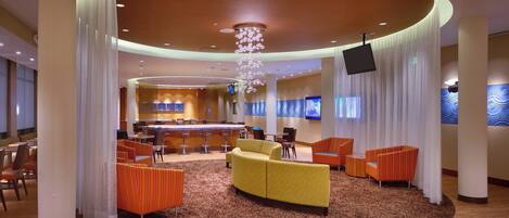 Een hotel lobby met een centraal zitgedeelte, een bar en een televisiescherm.