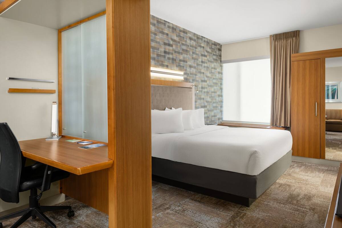 A hotel room with a bed, a desk, a chair, a wardrobe, and a large window.
