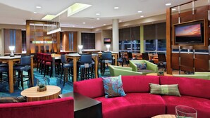 A modern hotel lobby with a red sofa, multiple seating areas, a TV, and a staircase. - SpringHill Suites Pensacola (Pensacola)
