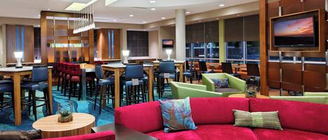 A modern hotel lobby with a red sofa, multiple seating areas, a TV, and a staircase.