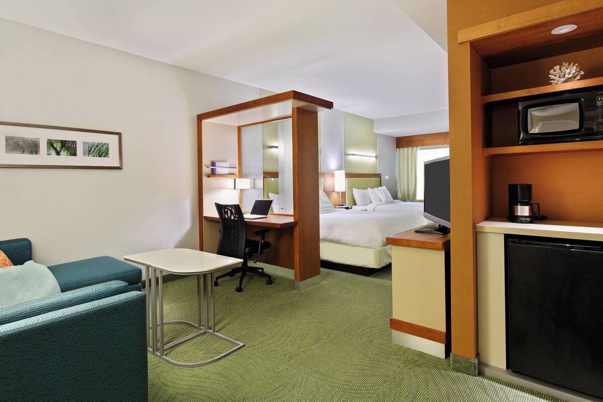 A hotel room with a bed, a desk with a chair, a small table, and a microwave.