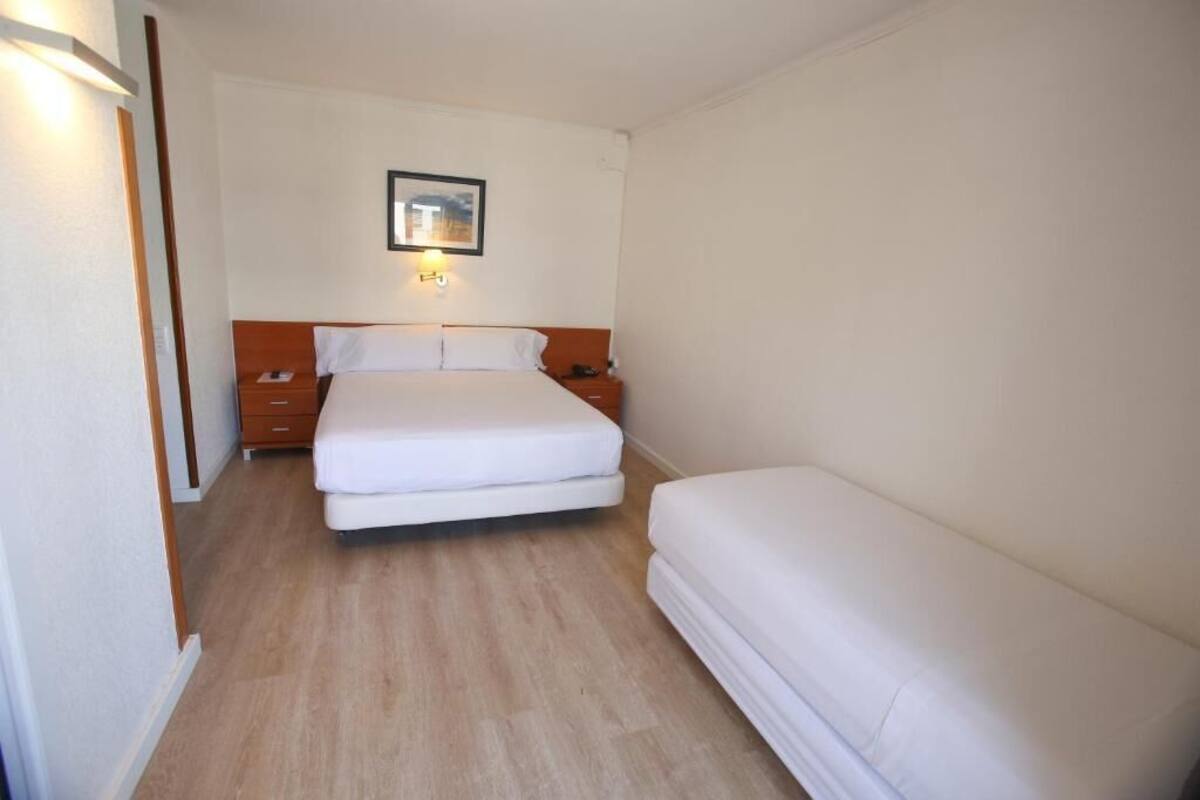 Habitación de hotel con una cama individual, una mesita de noche y una lámpara fijada a la pared.
