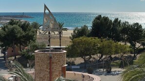Vista costera con una estructura metálica decorativa, palmeras y cielo despejado.