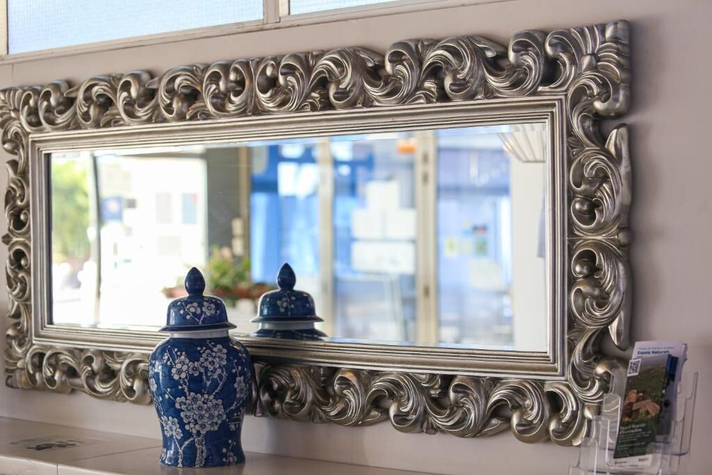 Een spiegel met een sierlijk zilveren frame, een blauwe vaas met bloemmotieven, en een klein blauw-wit keramieken potje.