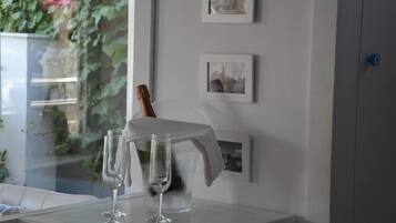 Una habitación moderna con una mesa de vidrio, dos copas de vino, una botella de champán y cuadros enmarcados en la pared.