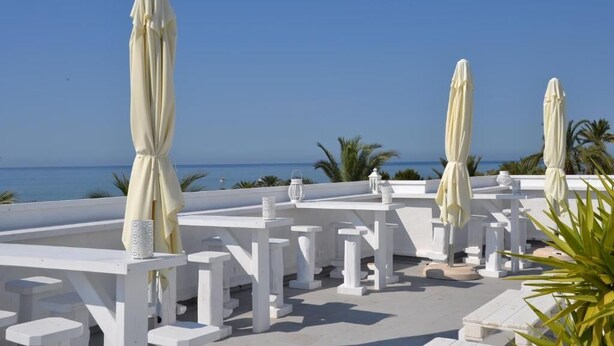 Una terraza en la azotea con mesas y sombrillas blancas, con vistas al mar.