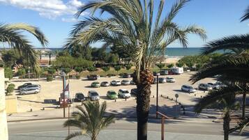 Un estacionamiento con varios coches, palmeras y una playa al fondo.