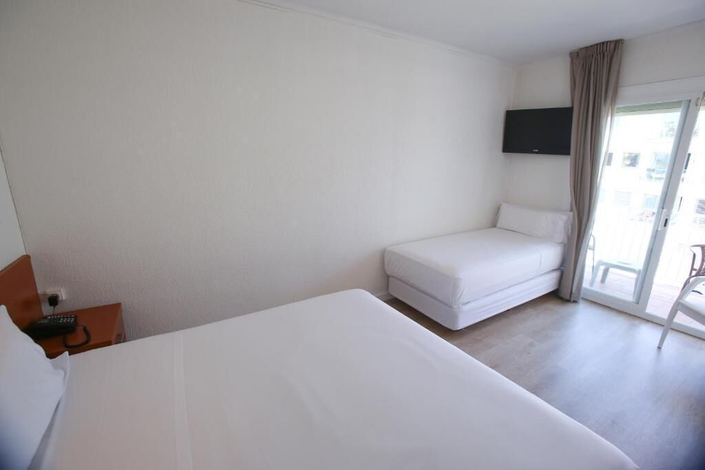 A hotel room with a large bed, a smaller sofa, a TV mounted on the wall, and a sliding glass door to the outside.