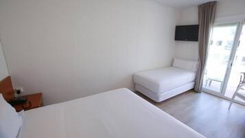 A hotel room with a large bed, a smaller sofa, a TV mounted on the wall, and a sliding glass door to the outside.