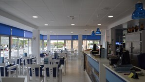 Un moderno vestíbulo de hotel con decoración blanca y azul, un mostrador de recepción y un comedor con sillas y mesas blancas.