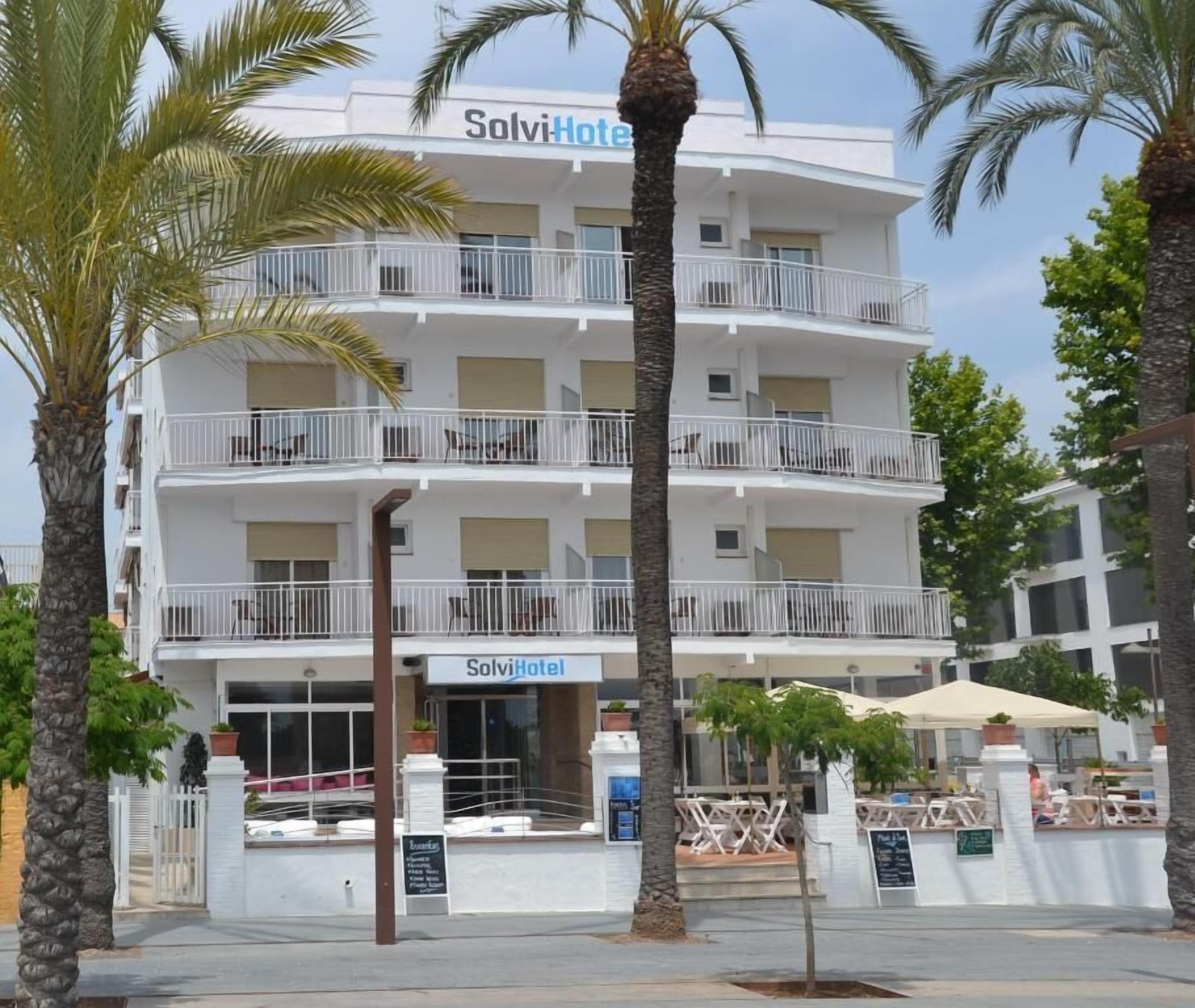 A multi-story hotel with balconies, palm trees, and outdoor seating.