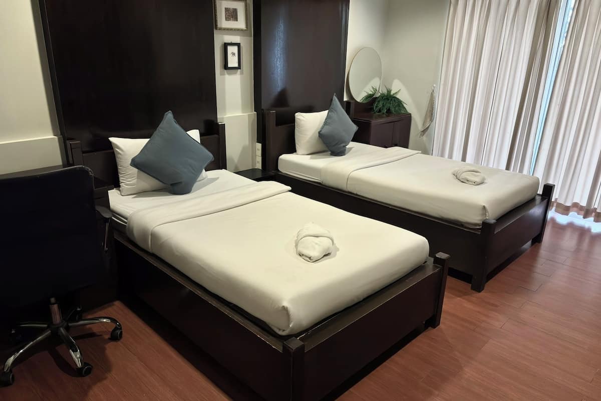 Two single beds with dark wooden frames and white bedding, a small desk with a chair, and a mirror on a bedside table.