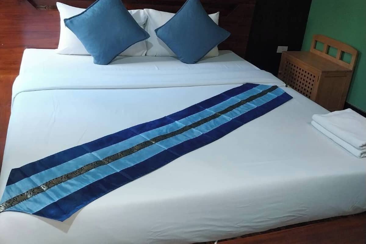 A neatly made bed with a blue and white striped bedspread, two blue pillows, and a wooden headboard.